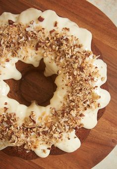 a frosted donut with white icing and chopped nuts on a wooden platter