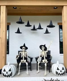 two skeletons sitting on chairs in front of a white wall with black hats and pumpkins