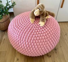 a stuffed animal sitting on top of a pink crocheted poufce cushion