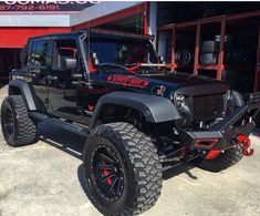 a black jeep is parked in front of a building with red lettering on the side