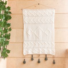 a white wall hanging on the side of a brick building next to a potted plant