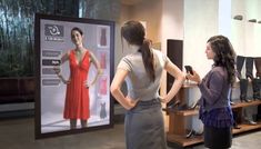 two women standing in front of a tv screen with dresses on it and one woman looking at the television