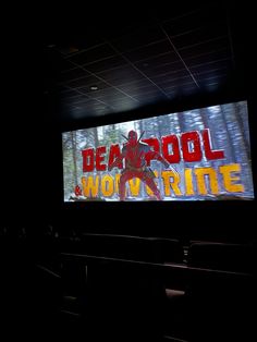 a large screen with the words deadpool and wolverine on it in a dark room