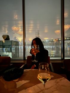 a woman sitting at a table with a wine glass in front of her and a view of the city