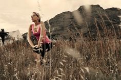 a woman in a pink top is standing in tall grass with mountains in the background