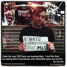 a man holding up a sign in front of a drum set with words written on it