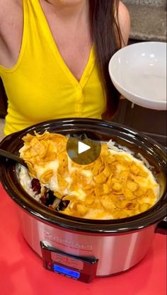 a woman sitting in front of a crock pot filled with food