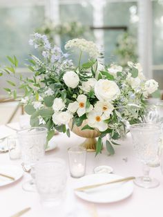 a vase filled with white flowers sitting on top of a table next to glasses and plates