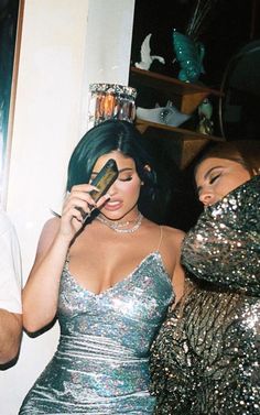 two women dressed in sequins are talking on their cell phones and one is holding a phone up to her ear