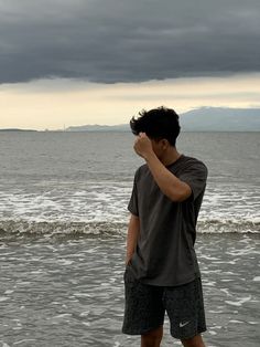 a man standing in the water with his hand on his head while looking at the ocean