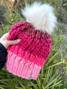 a hand holding a pink and white knitted hat