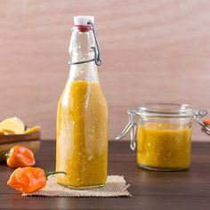 a glass bottle filled with mustard sitting on top of a wooden table next to peppers