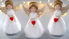 three angel figurines with red hearts in their hands and lights behind them on a table