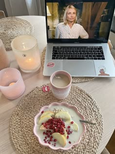 a laptop computer sitting on top of a wooden table next to a plate with fruit