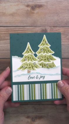 someone holding up a christmas card with pine trees on the front and green stripes on the back