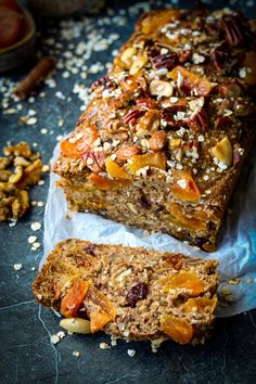 a loaf of fruit and nut bread on top of wax paper next to some nuts