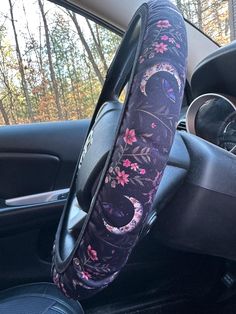 the steering wheel cover is decorated with pink and purple flowers on black fabric, along with an intricate floral design