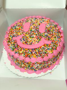 a pink frosted cake with sprinkles and a smiley face on it