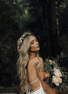 a woman wearing a white dress holding a bouquet of flowers and greenery in her hand