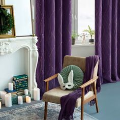 a living room with purple curtains and a chair in front of a fireplace filled with candles