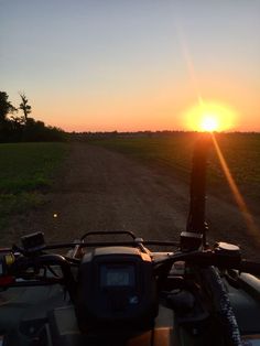 the sun is setting over a dirt road with a motorcycle parked on it's side