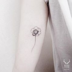 a single flower tattoo on the left inner arm, with a small white flower in the middle