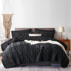 a bed with black comforter and pillows in a room next to a night stand