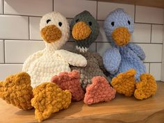 three crocheted stuffed birds sitting on top of a wooden counter next to a white tiled wall