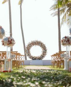 an outdoor ceremony setup with flowers and wreaths on the back wall, surrounded by palm trees