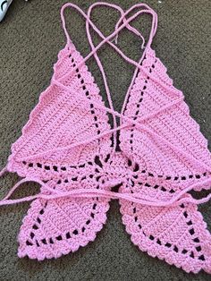 a pink crocheted bralet laying on the floor next to a pair of scissors