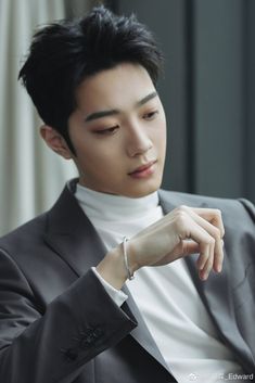 a man in a suit and white turtle neck shirt looking down at his wrist watch