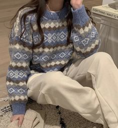 a woman is sitting on the floor talking on her cell phone while wearing a blue sweater and white pants