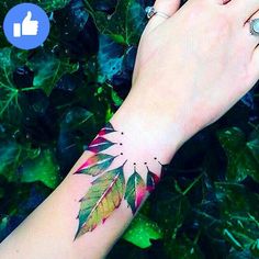 a woman's hand with a tattoo on her wrist that has leaves painted on it