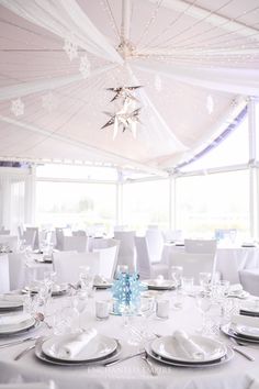 the tables are set for an event with white linens and snowflakes hanging from the ceiling