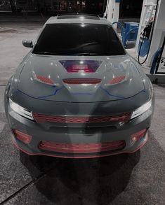 the front end of a gray car at a gas station with no one around it