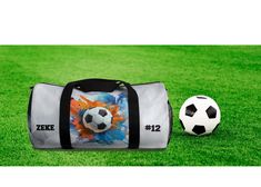 a soccer ball sitting on top of a field next to a duffle bag with an image of a soccer ball painted on it