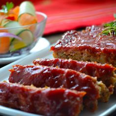 meatloaf on a white plate next to a bowl of vegetables