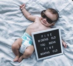 a baby laying on top of a blanket holding a sign