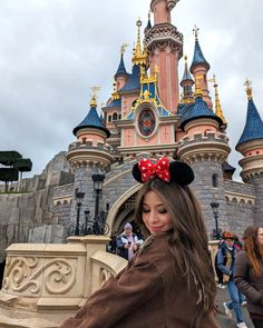 a woman standing in front of a castle with a minnie mouse ears on her head