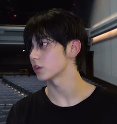 a young man with black hair standing in front of an empty auditorium seat looking at the camera