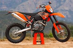 an orange dirt bike parked on top of a red stand in front of some mountains