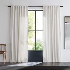 a white curtain hanging in front of a window with a black rug on the floor