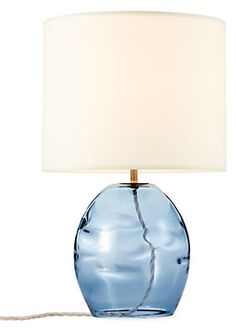 a blue glass table lamp with a white shade on the base and a cord attached to it