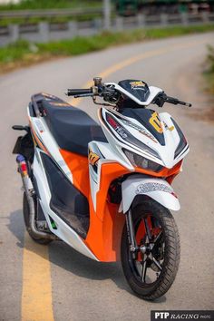 an orange and white motorcycle parked on the side of a road next to a fence