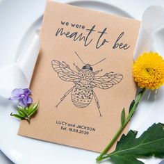 a card with a bee drawn on it next to some flowers and green leafy stems