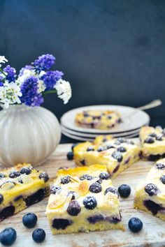 slices of blueberry cheesecake on a cutting board with flowers and plates in the background