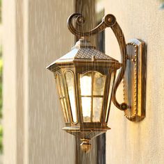 an old fashioned street light on the side of a building with rain coming down from it