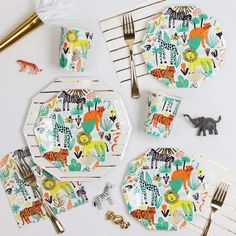 a table set with plates, forks and napkins decorated with colorful jungle animal designs