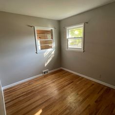 empty room with hard wood flooring and two windows in the corner on each side