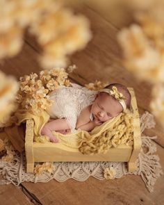 a baby sleeping in a wooden box with yellow flowers on the table next to it